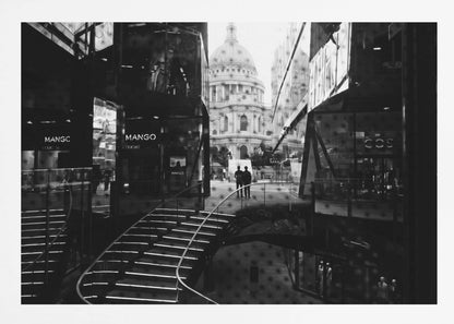 A framed, black and white photograph capturing a layered urban scene. The view, seen through a window with reflections of a curved, lit staircase, shows two people walking towards a large domed cathedral framed by modern glass buildings. Wall Art
