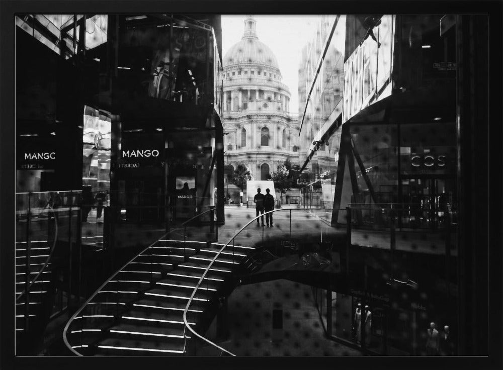 A framed, black and white photograph capturing a layered urban scene. The view, seen through a window with reflections of a curved, lit staircase, shows two people walking towards a large domed cathedral framed by modern glass buildings. Wall Art