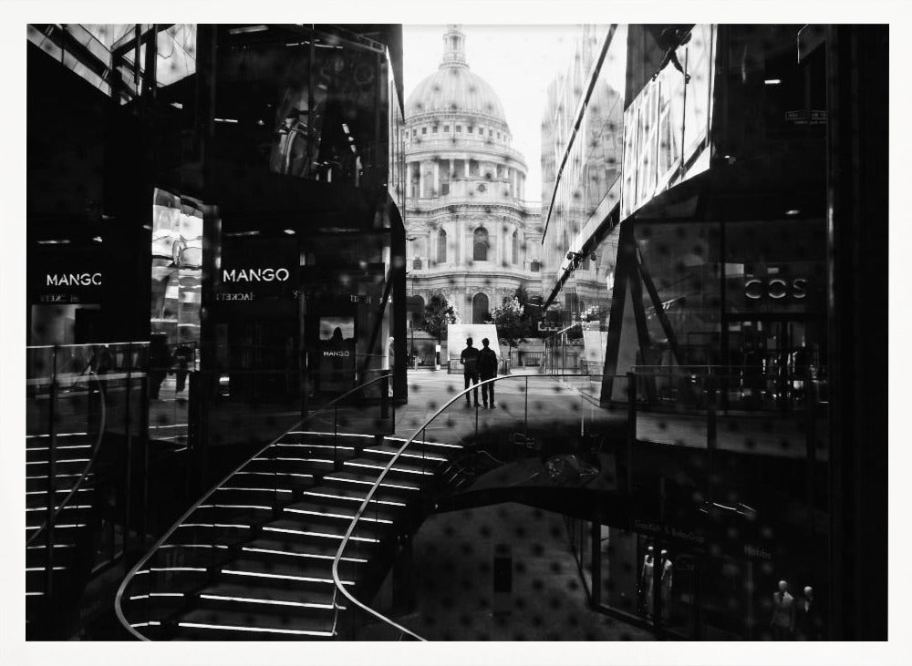 A framed, black and white photograph capturing a layered urban scene. The view, seen through a window with reflections of a curved, lit staircase, shows two people walking towards a large domed cathedral framed by modern glass buildings. Wall Art