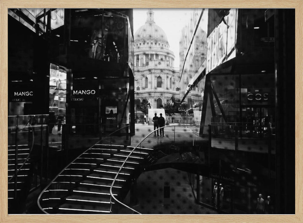 A framed, black and white photograph capturing a layered urban scene. The view, seen through a window with reflections of a curved, lit staircase, shows two people walking towards a large domed cathedral framed by modern glass buildings. Wall Art