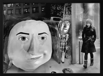 A surreal black and white photograph with a silver frame, featuring a giant, cartoonish head of a historical figure reflected in a window, juxtaposed with a young woman in a winter coat and beanie walking down a city sidewalk. Wall Art