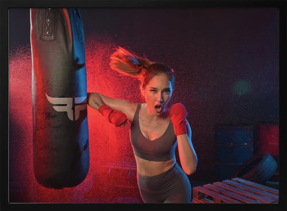 An athletic woman with her hair in a ponytail and red hand wraps fiercely punches a black heavy bag, her mouth open mid-shout. The scene is dramatically lit with red and blue light, and water droplets spray through the air from the impact. Poster