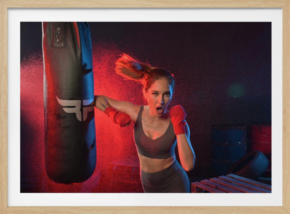 An athletic woman with her hair in a ponytail and red hand wraps fiercely punches a black heavy bag, her mouth open mid-shout. The scene is dramatically lit with red and blue light, and water droplets spray through the air from the impact. Poster