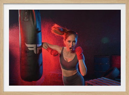 An athletic woman with her hair in a ponytail and red hand wraps fiercely punches a black heavy bag, her mouth open mid-shout. The scene is dramatically lit with red and blue light, and water droplets spray through the air from the impact. Poster