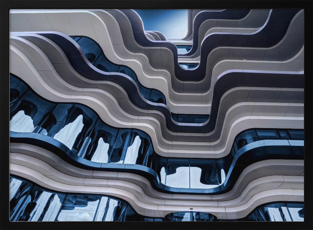A low-angle view of a modern building with a striking, wavy facade. Alternating bands of light and dark grey create a fluid, ribbon-like pattern, with curved glass windows reflecting the deep blue sky. Artwork