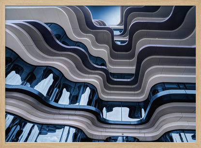 A low-angle view of a modern building with a striking, wavy facade. Alternating bands of light and dark grey create a fluid, ribbon-like pattern, with curved glass windows reflecting the deep blue sky. Artwork