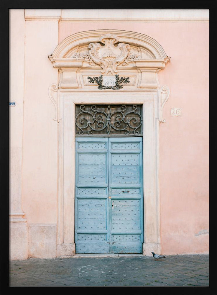 A light blue, studded double door set into a pale pink wall. The doorway is framed in white stone with an ornate pediment and a decorative wrought-iron transom window above the door. A single pigeon stands on the cobblestone pavement in front. Print