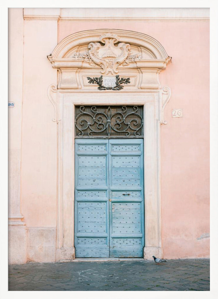 A light blue, studded double door set into a pale pink wall. The doorway is framed in white stone with an ornate pediment and a decorative wrought-iron transom window above the door. A single pigeon stands on the cobblestone pavement in front. Print