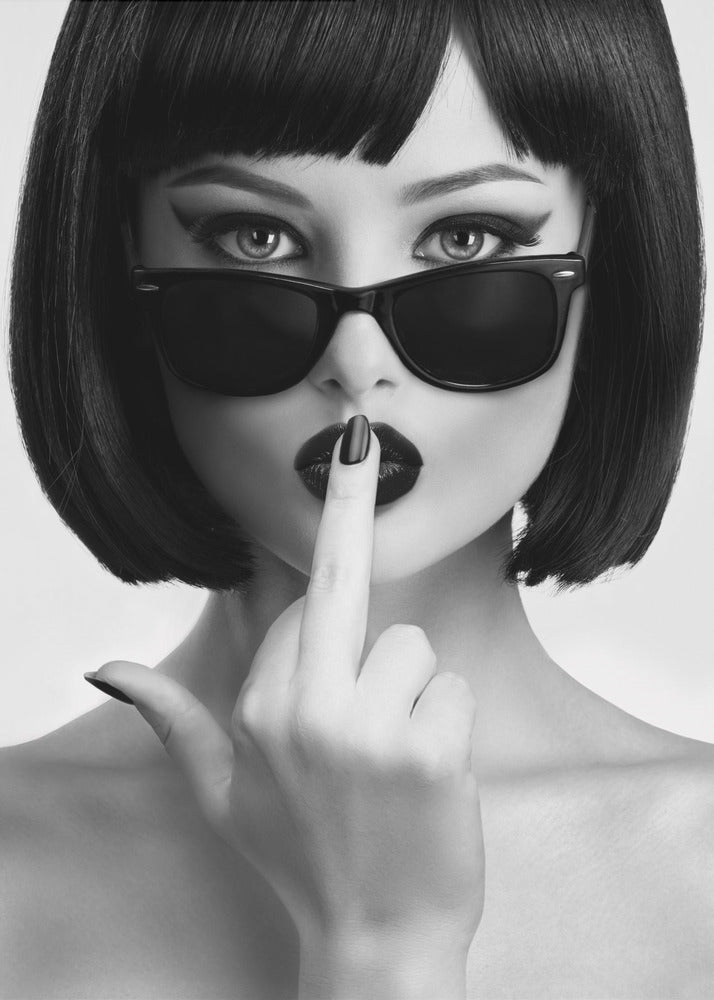 A striking black and white portrait of a woman with a sharp bob haircut, sunglasses, and bold makeup. She holds one finger with a black-painted nail up to her dark lips, making a 'shushing' gesture. Poster