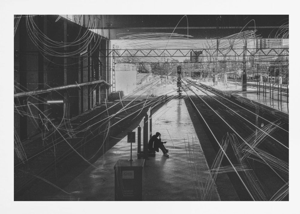 A framed, high-contrast black and white photograph of a person sitting alone on a deserted train platform, with tracks stretching into the distance. The entire scene is overlaid with frenetic white scribbles, creating an abstract and moody effect. Artwork