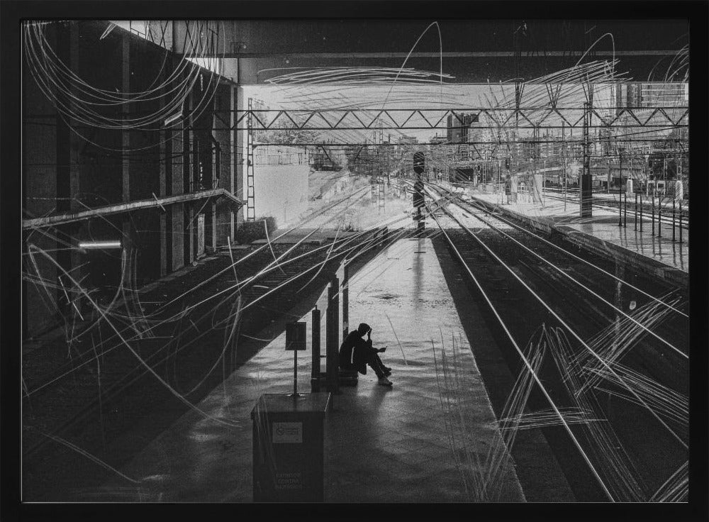A framed, high-contrast black and white photograph of a person sitting alone on a deserted train platform, with tracks stretching into the distance. The entire scene is overlaid with frenetic white scribbles, creating an abstract and moody effect. Artwork