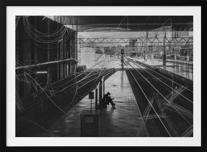A framed, high-contrast black and white photograph of a person sitting alone on a deserted train platform, with tracks stretching into the distance. The entire scene is overlaid with frenetic white scribbles, creating an abstract and moody effect. Artwork