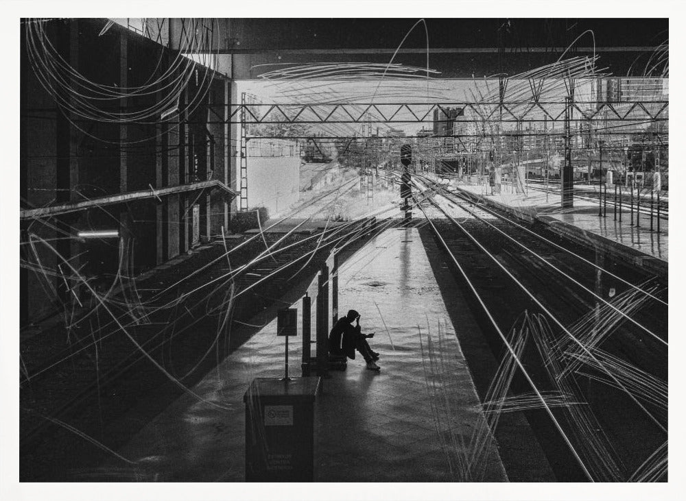A framed, high-contrast black and white photograph of a person sitting alone on a deserted train platform, with tracks stretching into the distance. The entire scene is overlaid with frenetic white scribbles, creating an abstract and moody effect. Artwork