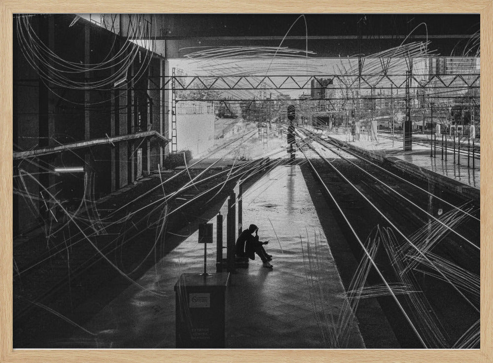 A framed, high-contrast black and white photograph of a person sitting alone on a deserted train platform, with tracks stretching into the distance. The entire scene is overlaid with frenetic white scribbles, creating an abstract and moody effect. Artwork