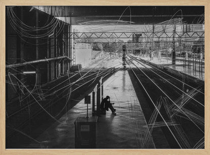 A framed, high-contrast black and white photograph of a person sitting alone on a deserted train platform, with tracks stretching into the distance. The entire scene is overlaid with frenetic white scribbles, creating an abstract and moody effect. Artwork