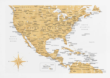 A stylized map of North and Central America and the Caribbean, featuring gold-colored landmasses on a light gray, textured background. Countries, states, and major cities are labeled in black text. A compass rose is shown in the lower-left corner. The entire map is enclosed in a light gray frame. Decor