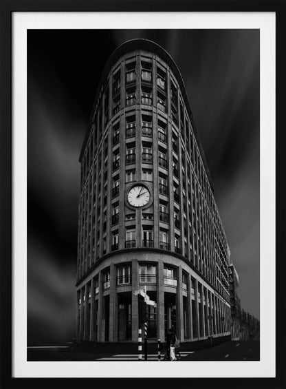 A dramatic low-angle, black and white photograph of a large, curved corner building with a prominent clock on its facade. The sky is dark with a motion blur effect, making the building appear grand and imposing. Artwork