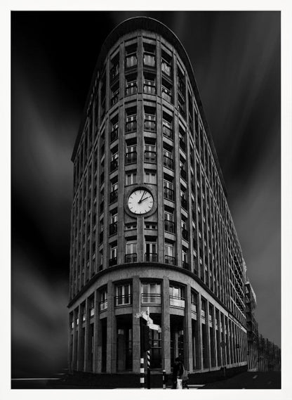 A dramatic low-angle, black and white photograph of a large, curved corner building with a prominent clock on its facade. The sky is dark with a motion blur effect, making the building appear grand and imposing. Artwork