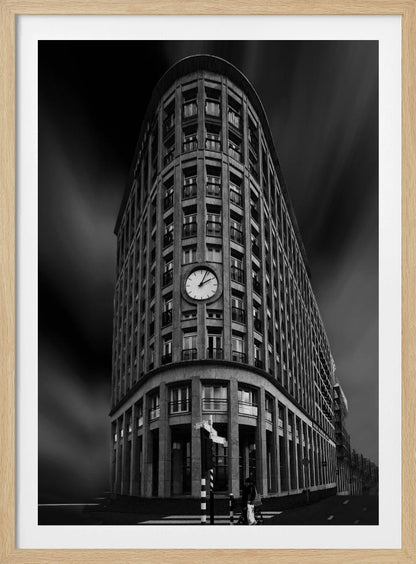 A dramatic low-angle, black and white photograph of a large, curved corner building with a prominent clock on its facade. The sky is dark with a motion blur effect, making the building appear grand and imposing. Artwork