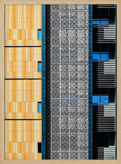 A vertical abstract architectural photograph showcasing the facade of a modern building, featuring a contrast of textures and colors: warm yellow vertical tiles on the left, an intricate white geometric screen in the center, and a dark section with vibrant blue windows on the right. Print