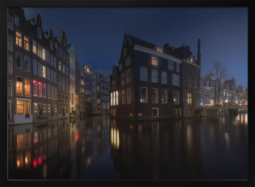 A framed photograph capturing a serene night view of an Amsterdam canal. Traditional Dutch houses with lit windows line the calm water, casting warm reflections under a deep blue twilight sky. Wall Art