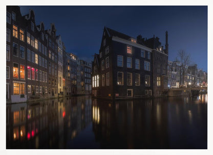 A framed photograph capturing a serene night view of an Amsterdam canal. Traditional Dutch houses with lit windows line the calm water, casting warm reflections under a deep blue twilight sky. Wall Art