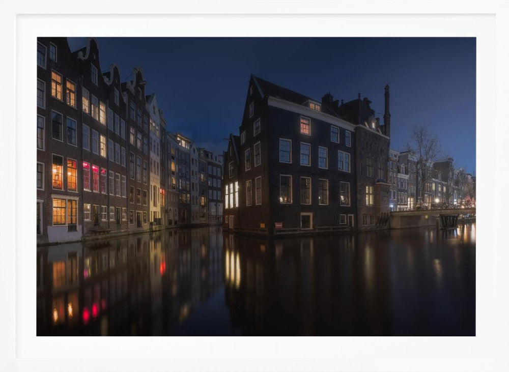 A framed photograph capturing a serene night view of an Amsterdam canal. Traditional Dutch houses with lit windows line the calm water, casting warm reflections under a deep blue twilight sky. Wall Art
