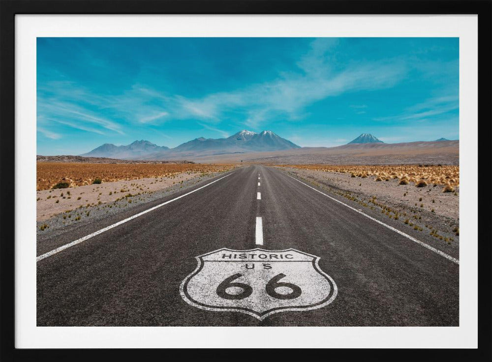 A framed photograph of the iconic Historic US Route 66 shield painted on a long, straight asphalt road that stretches through a desert landscape toward distant snow-capped mountains under a vibrant blue sky. Wall Art
