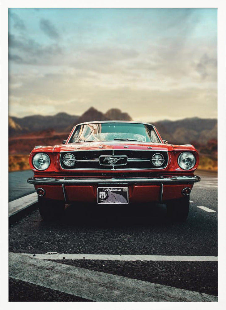 A low-angle, head-on shot of a vintage red Ford Mustang parked on an asphalt road. The iconic silver horse emblem is visible on the grille. In the background, a desert mountain range is blurred under a cloudy, muted sky. Poster