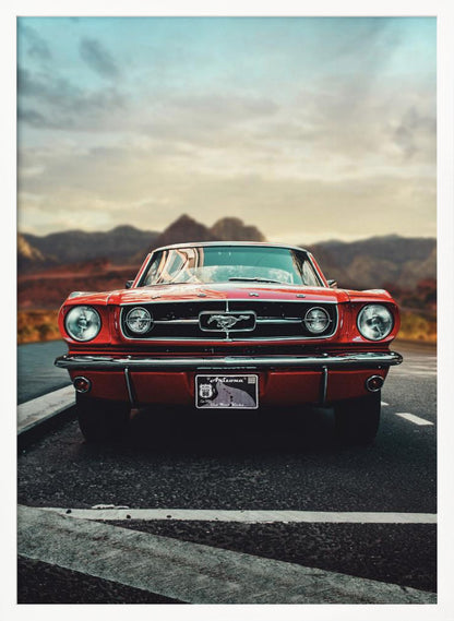 A low-angle, head-on shot of a vintage red Ford Mustang parked on an asphalt road. The iconic silver horse emblem is visible on the grille. In the background, a desert mountain range is blurred under a cloudy, muted sky. Poster