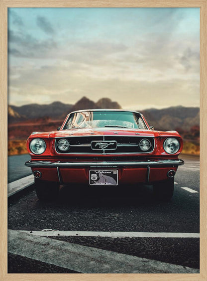 A low-angle, head-on shot of a vintage red Ford Mustang parked on an asphalt road. The iconic silver horse emblem is visible on the grille. In the background, a desert mountain range is blurred under a cloudy, muted sky. Poster