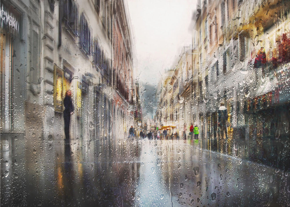 An impressionistic painting of a city street on a rainy day, viewed as if through a window covered in water droplets. The scene is blurred and atmospheric, with the wet pavement reflecting the muted colors of the buildings and distant figures. The artwork is presented in a silver frame. Decor