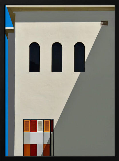 A minimalist photograph of a cream-colored building facade with a sharp diagonal shadow. Three black arched windows are arranged horizontally, and below them, a colorful grid of red, orange, and white panels. A vibrant blue vertical stripe is visible on the far left edge. Wall Art