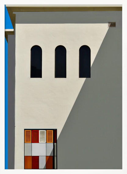 A minimalist photograph of a cream-colored building facade with a sharp diagonal shadow. Three black arched windows are arranged horizontally, and below them, a colorful grid of red, orange, and white panels. A vibrant blue vertical stripe is visible on the far left edge. Wall Art