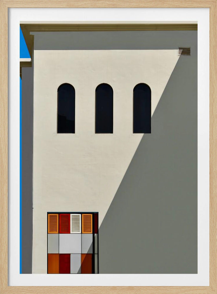 A minimalist photograph of a cream-colored building facade with a sharp diagonal shadow. Three black arched windows are arranged horizontally, and below them, a colorful grid of red, orange, and white panels. A vibrant blue vertical stripe is visible on the far left edge. Wall Art