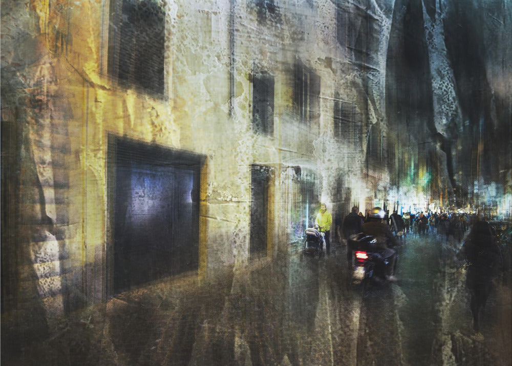 A framed abstract digital artwork depicting a busy, narrow city street at night. The image has a heavily textured, painterly style, with blurred motion effects. A weathered, yellow-lit building is on the left, while the street on the right is filled with indistinct figures of people and a motorcycle, with city lights glowing in the distance. Wall Art