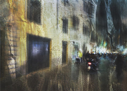 A framed abstract digital artwork depicting a busy, narrow city street at night. The image has a heavily textured, painterly style, with blurred motion effects. A weathered, yellow-lit building is on the left, while the street on the right is filled with indistinct figures of people and a motorcycle, with city lights glowing in the distance. Wall Art