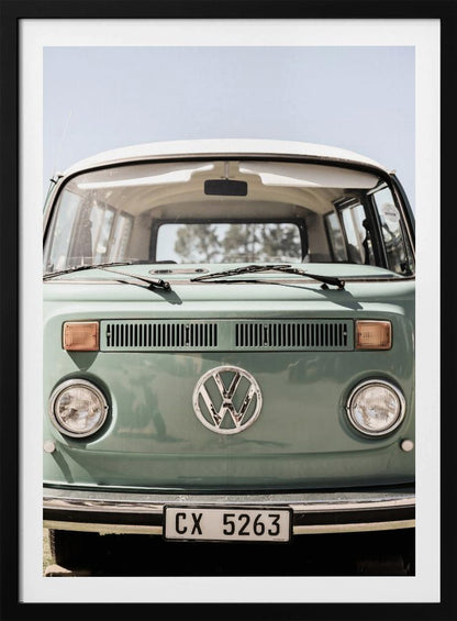 A close-up front view of a vintage sage green Volkswagen bus with a white roof. The iconic VW logo is on the front, with round headlights and a European license plate, set against a pale blue sky. Print