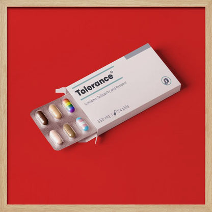 A framed conceptual art piece on a bright red background. It features a white medicine box labeled 'Tolerance', with a blister pack of pills emerging. Most pills are in various skin tones, but one is a rainbow pride flag and another is a transgender pride flag. Artwork
