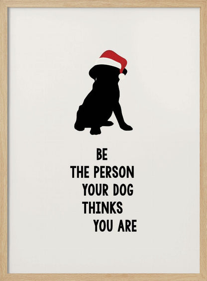 A framed art print featuring a black silhouette of a dog wearing a red Santa hat on an off-white background. Below the dog is the motivational quote, 'BE THE PERSON YOUR DOG THINKS YOU ARE' in black block letters. Decor