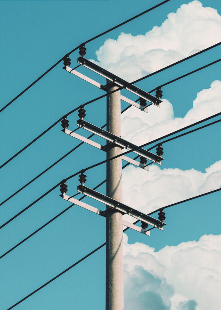 A low-angle photograph of a concrete utility pole with black power lines stretching diagonally across the frame against a vibrant blue sky with fluffy white clouds. Decor