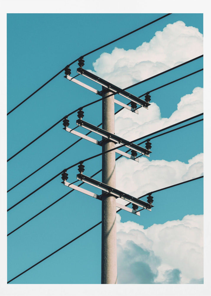 A low-angle photograph of a concrete utility pole with black power lines stretching diagonally across the frame against a vibrant blue sky with fluffy white clouds. Decor