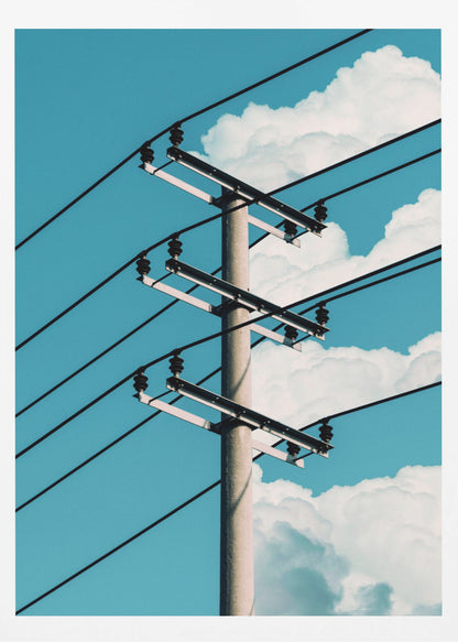 A low-angle photograph of a concrete utility pole with black power lines stretching diagonally across the frame against a vibrant blue sky with fluffy white clouds. Decor