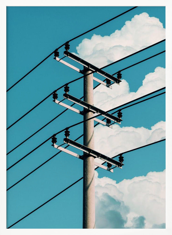 A low-angle photograph of a concrete utility pole with black power lines stretching diagonally across the frame against a vibrant blue sky with fluffy white clouds. Decor