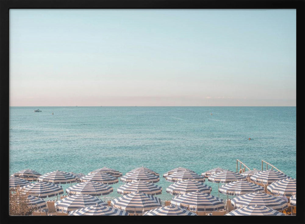 A high-angle photograph of a beach packed with blue and white striped umbrellas, with the turquoise ocean stretching out to a pale blue sky in the background. The entire image is enclosed in a silver frame. Poster