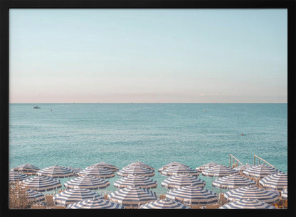 A high-angle photograph of a beach packed with blue and white striped umbrellas, with the turquoise ocean stretching out to a pale blue sky in the background. The entire image is enclosed in a silver frame. Poster