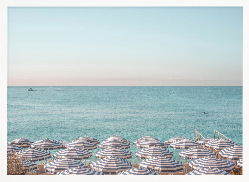 A high-angle photograph of a beach packed with blue and white striped umbrellas, with the turquoise ocean stretching out to a pale blue sky in the background. The entire image is enclosed in a silver frame. Poster