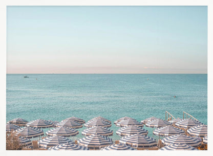 A high-angle photograph of a beach packed with blue and white striped umbrellas, with the turquoise ocean stretching out to a pale blue sky in the background. The entire image is enclosed in a silver frame. Poster