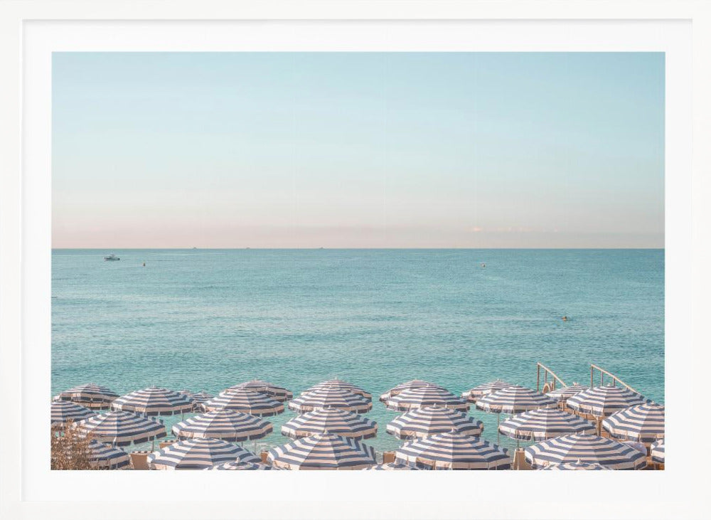 A high-angle photograph of a beach packed with blue and white striped umbrellas, with the turquoise ocean stretching out to a pale blue sky in the background. The entire image is enclosed in a silver frame. Poster
