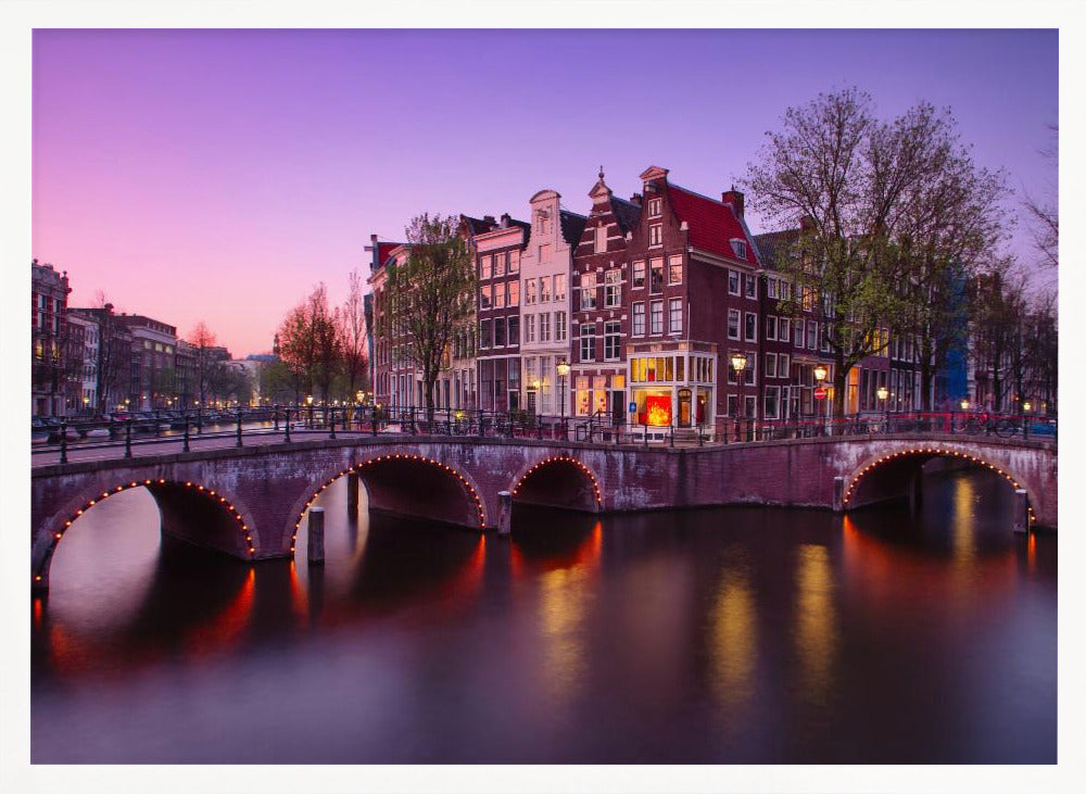A scenic view of an Amsterdam canal at twilight, with historic brick buildings and illuminated arched bridges reflected in the calm water under a vibrant pink and purple sky. Poster